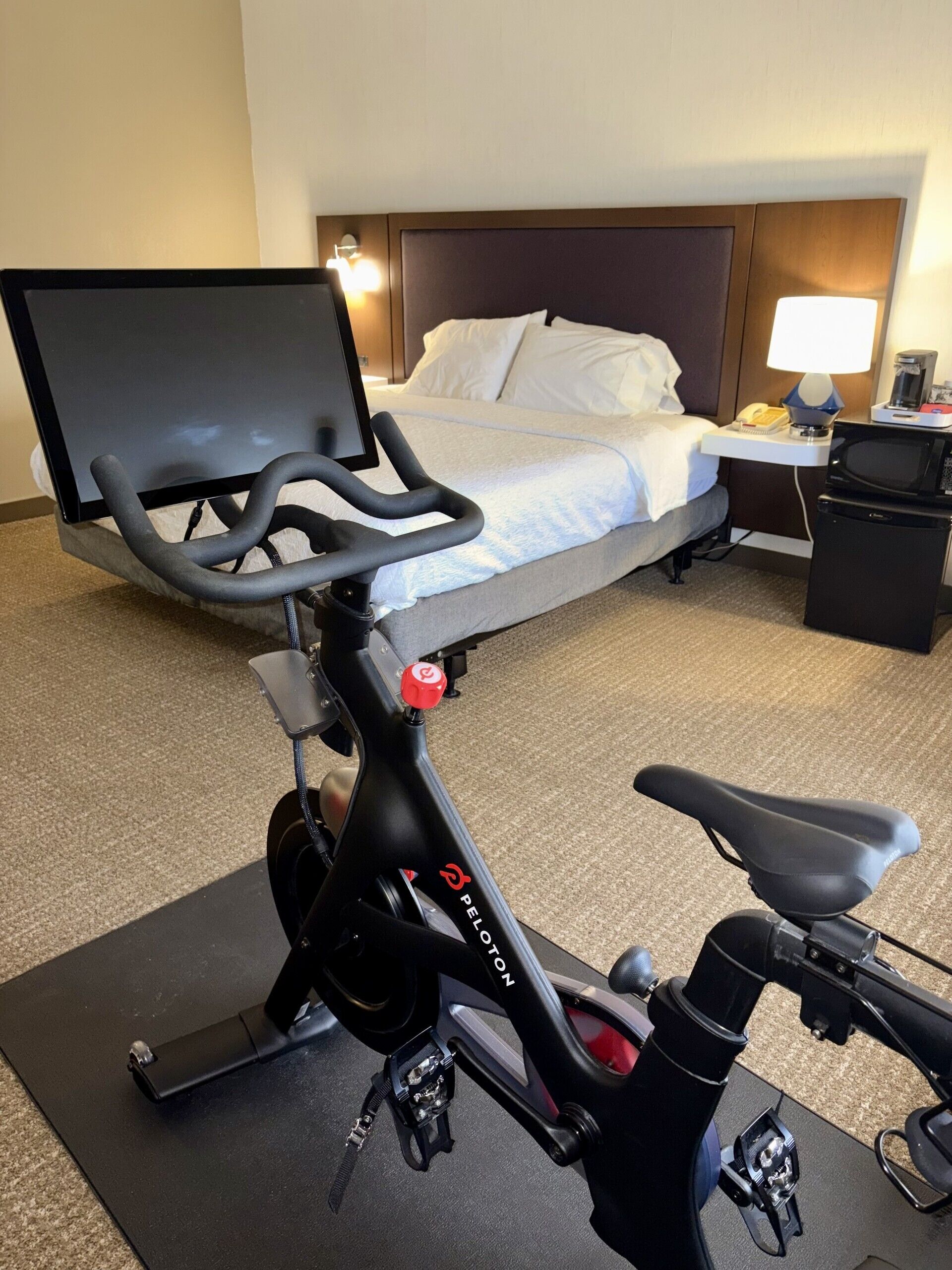 Una habitación de hotel con una cama, un escritorio con lámpara y una bicicleta estática.