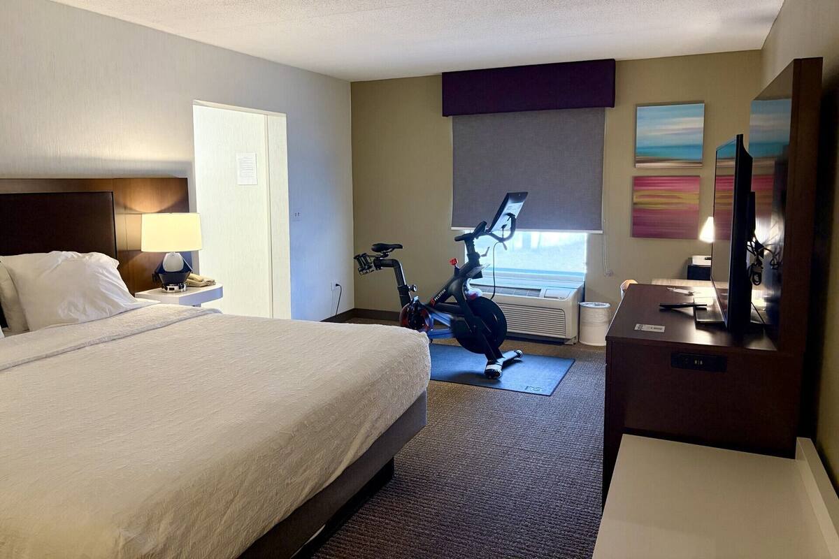 Hotelkamer met een bed, bureau, stoel, een hometrainer, televisie en raam met uitzicht.