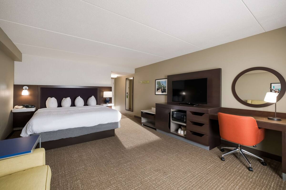 Een hotelkamer met een bed, een bureau met een computer, een televisie, een stoel en een spiegel.