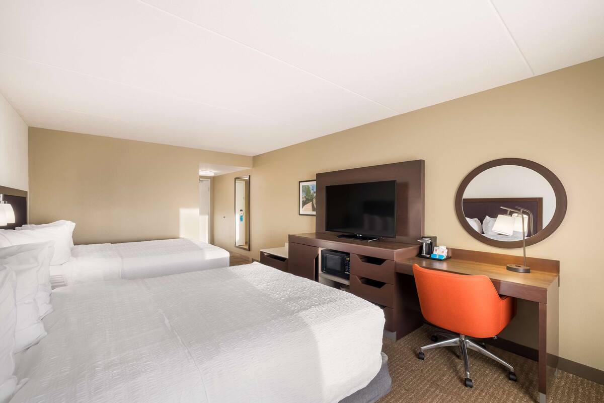 Een hotelkamer met twee bedden, een bureau met een computer, een televisie en een spiegel.