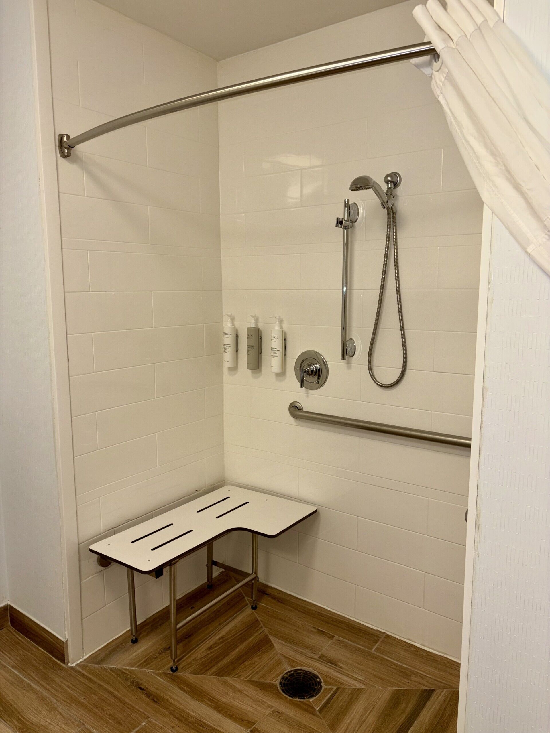 Zona de ducha con barra de apoyo, cabezal de ducha y ducha de mano.