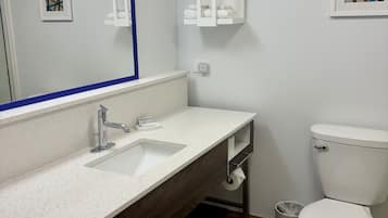 A bathroom with a white sink, a mirror with a blue frame, a toilet, and a small framed picture on the wall.