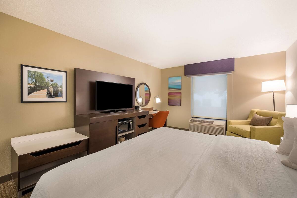 Hotelkamer met een groot bed, een flatscreen-tv, een bureau met stoel, een bank en een raam met uitzicht.