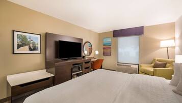 A hotel room with a large bed, a flat-screen TV, a desk with a chair, a sofa, and a window with a view.