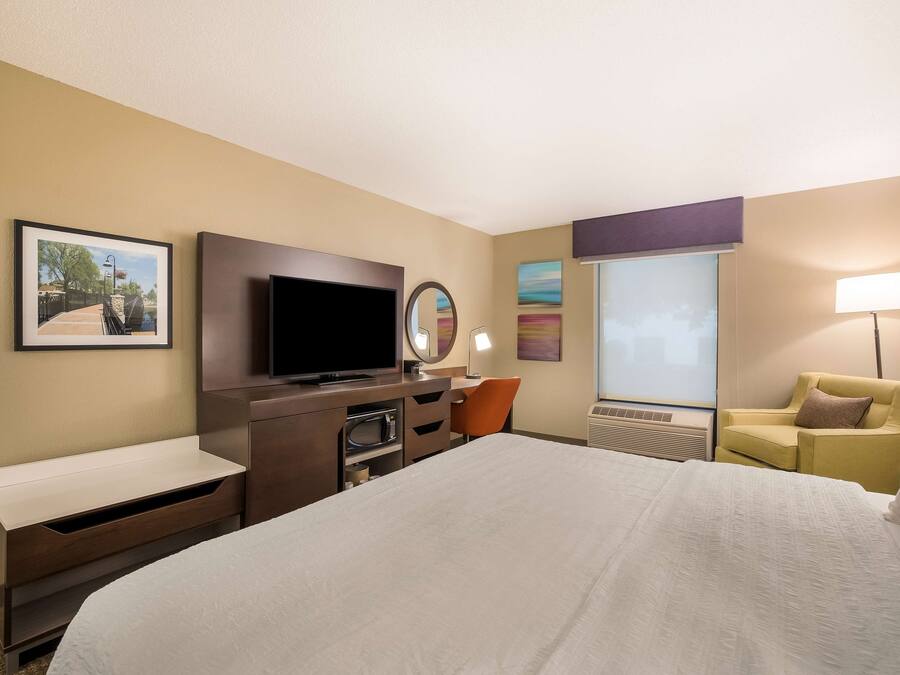 A hotel room with a large bed, a flat-screen TV, a desk with a chair, a sofa, and a window with a view.