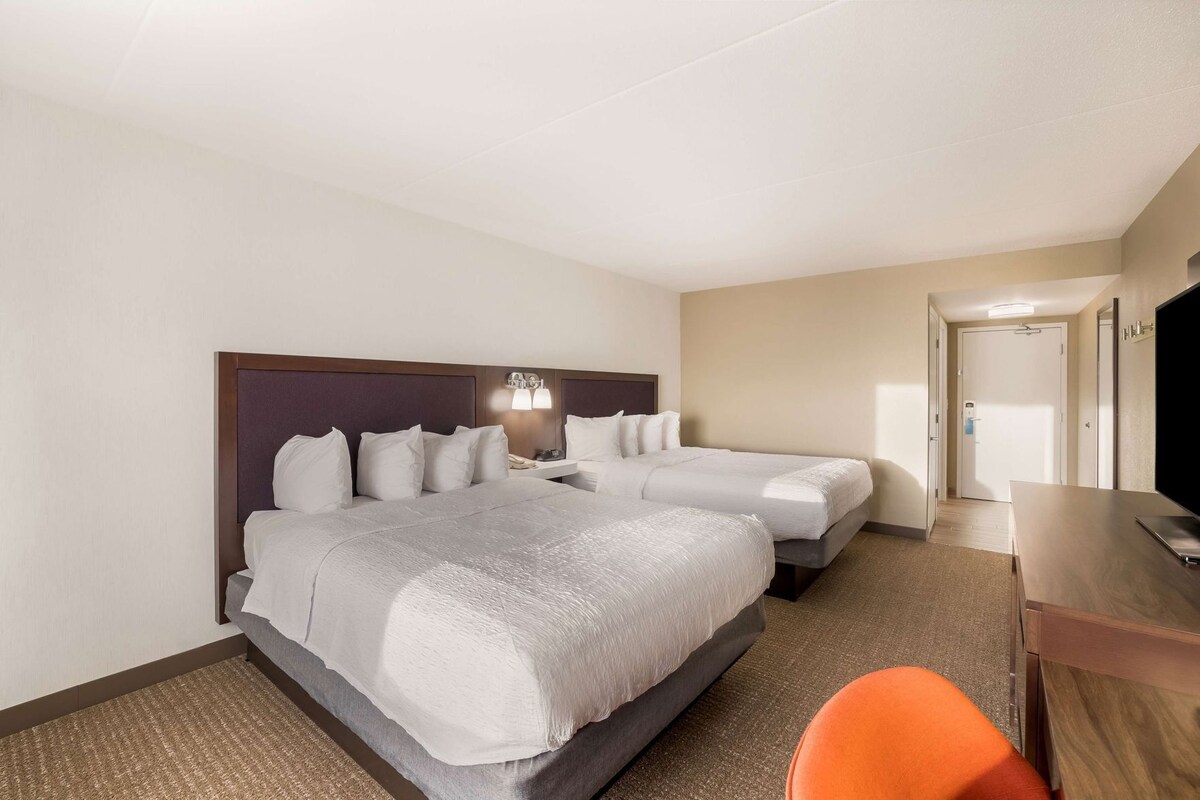 A hotel room with two beds, a desk, and a television.