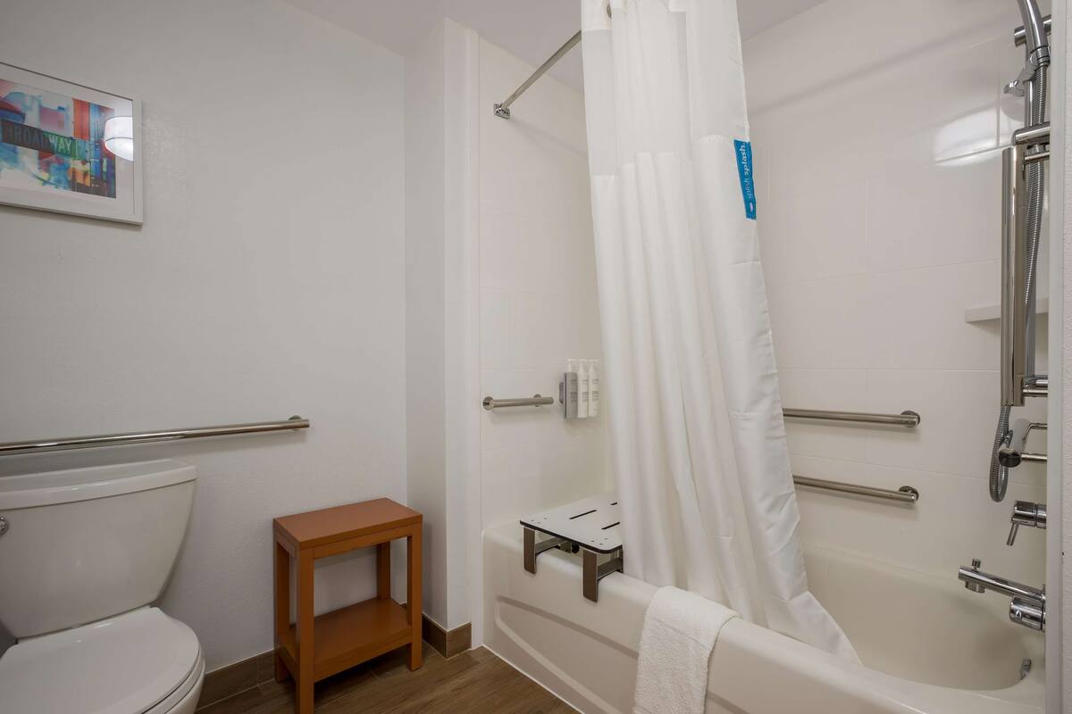 A bathroom with a shower, toilet, and a small wooden stool.