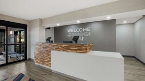 Un mostrador de recepción con un letrero que dice "WELCOME TO THE GARDEN", diseño moderno con detalles de madera y una puerta de vidrio que da acceso a un hall.