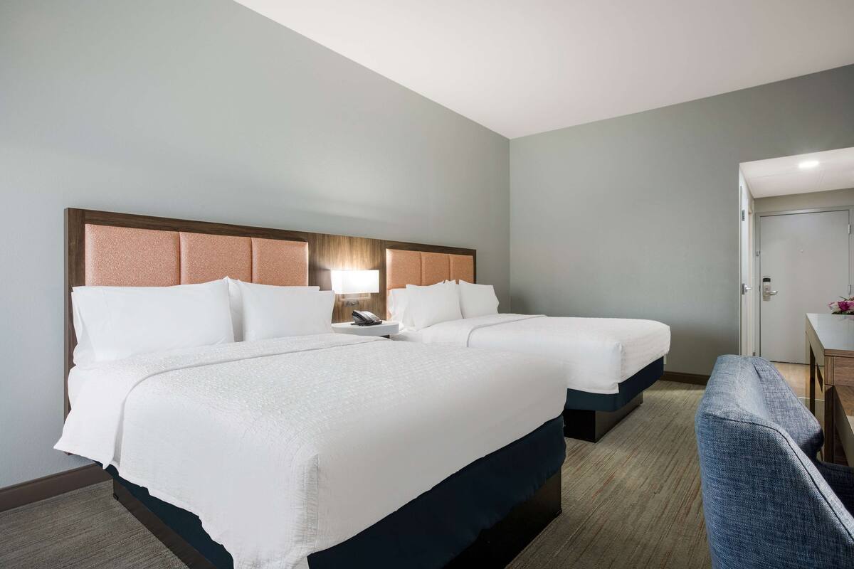 A hotel room with two beds, a desk, and a chair.