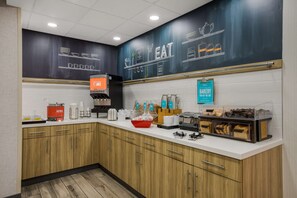 A modern kitchen with wooden cabinets, a coffee machine, and a chalkboard wall with food-related drawings.