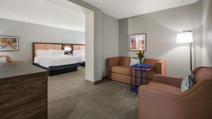 Una habitación de hotel con cama, escritorio, sofá y una mesita con un jarrón de flores.