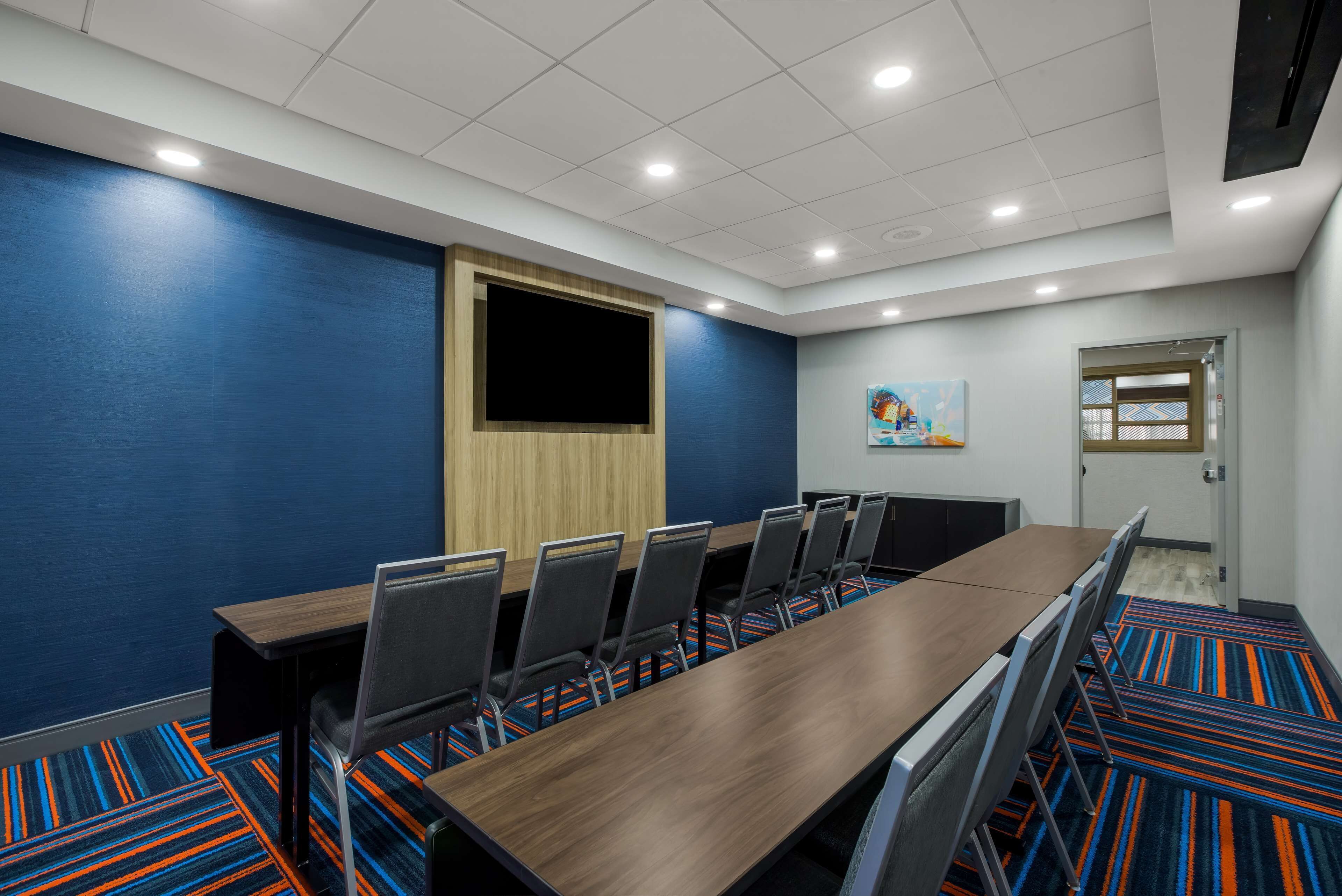 A conference room with a long table, chairs, and a large screen.