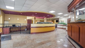 A spacious lobby with a curved reception desk, a tiled floor, and a high ceiling with recessed lighting. - Suburban Studios Florence I-95 (Florence)