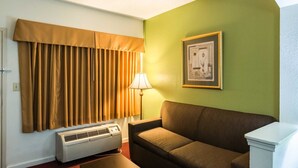 A room with a brown couch, a framed picture on the wall, a lamp, and a window with brown curtains. - Suburban Studios Florence I-95 (Florence)