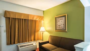 Quarto com sofá marrom, quadro pendurado na parede, luminária e janela com cortinas marrons.