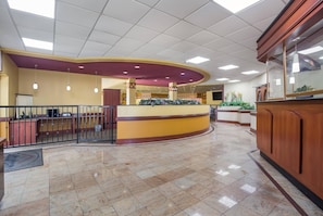 A spacious lobby with a curved reception desk, a tiled floor, and a ceiling with recessed lighting.