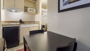 A compact kitchen with a microwave, refrigerator, and sink. There is a dining table with chairs and a framed picture on the wall. - Suburban Studios Florence I-95 (Florence)