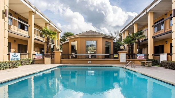 A swimming pool surrounded by a building with multiple balconies, clear skies, and warning signs. - Suburban Studios Florence I-95 (Florence)
