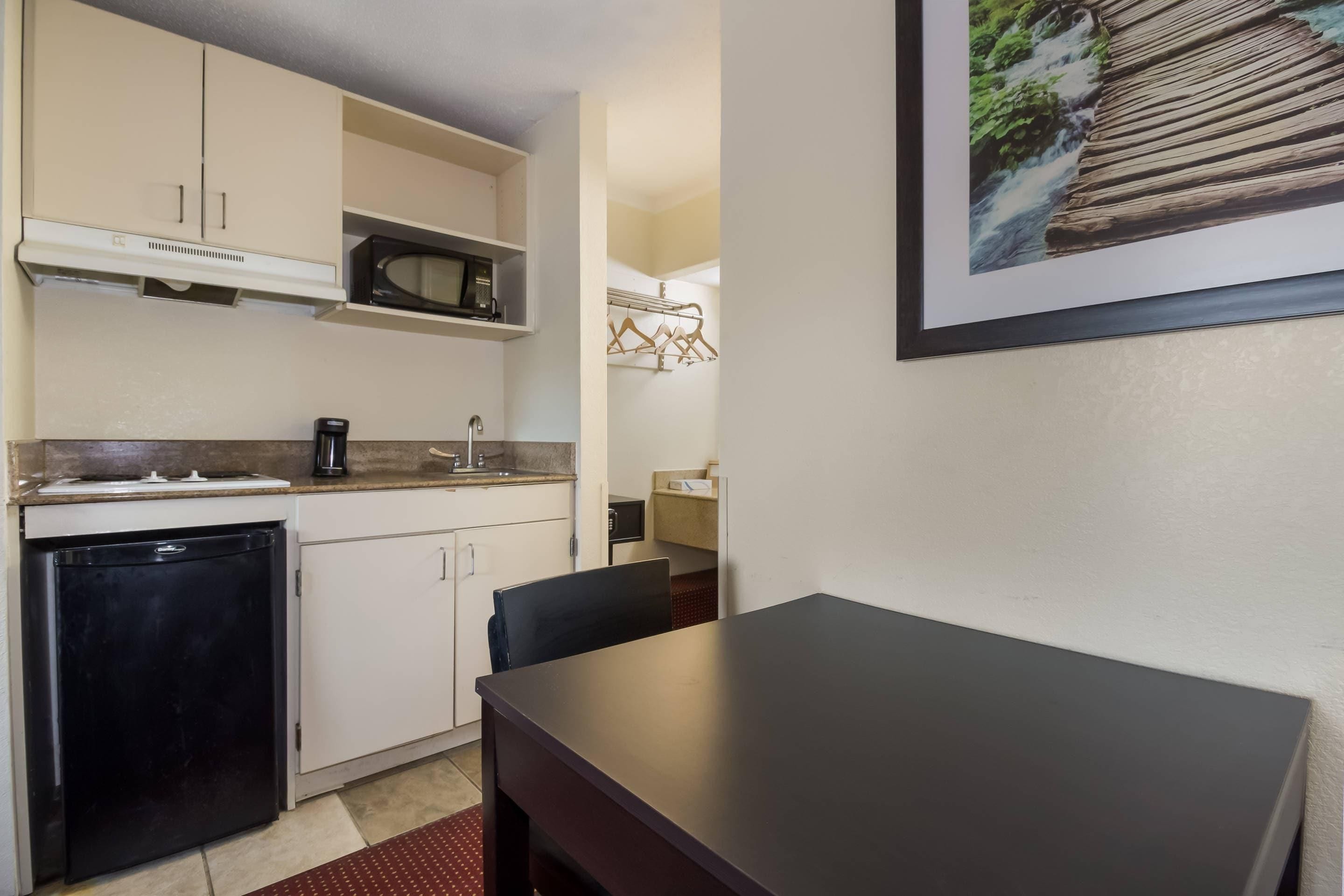 A compact kitchen with a refrigerator, microwave, and a coffee maker. There is a dining table with chairs and a framed picture on the wall.