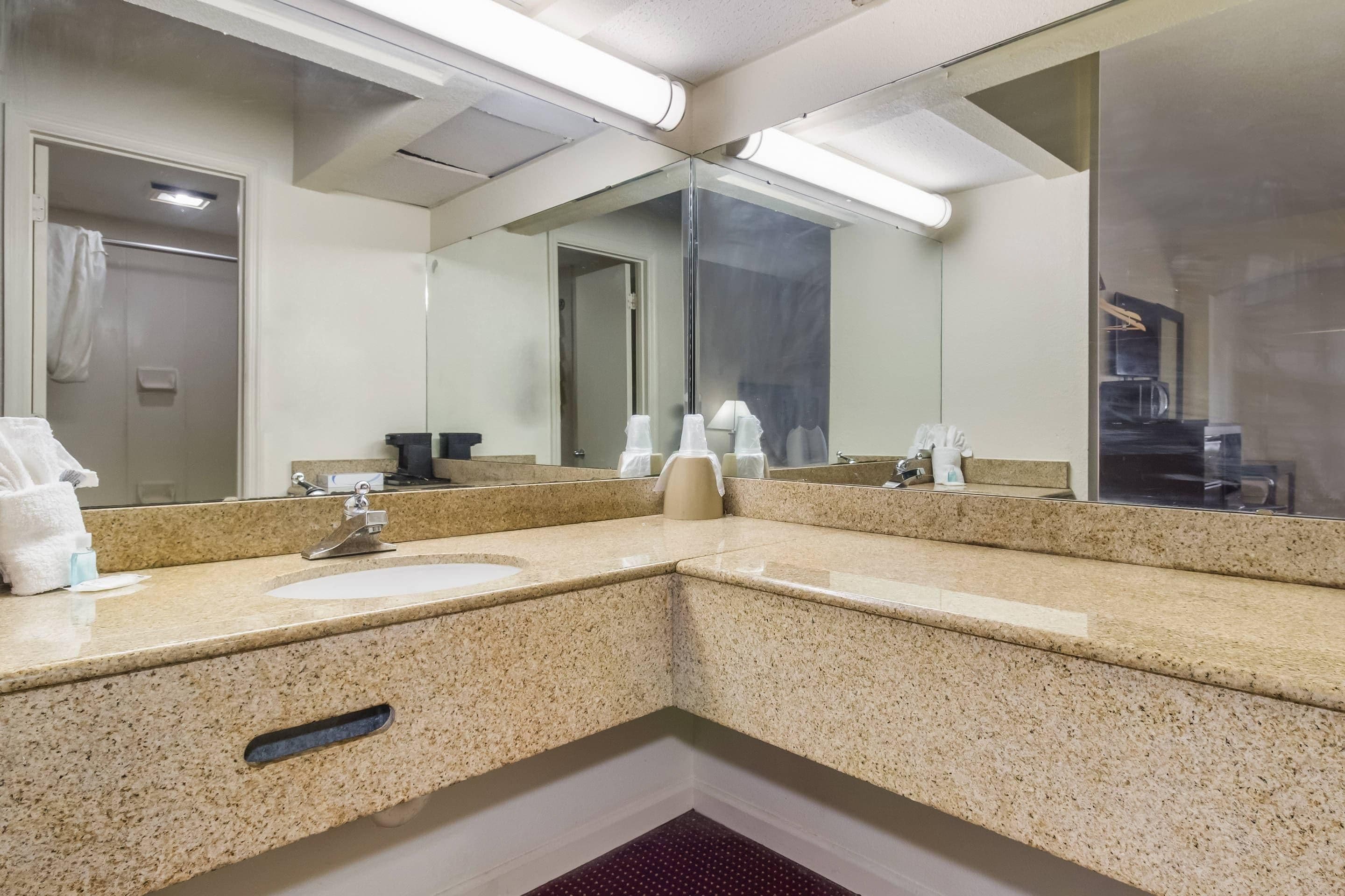 A hotel bathroom with a granite countertop, a sink, a mirror, and a shower area.