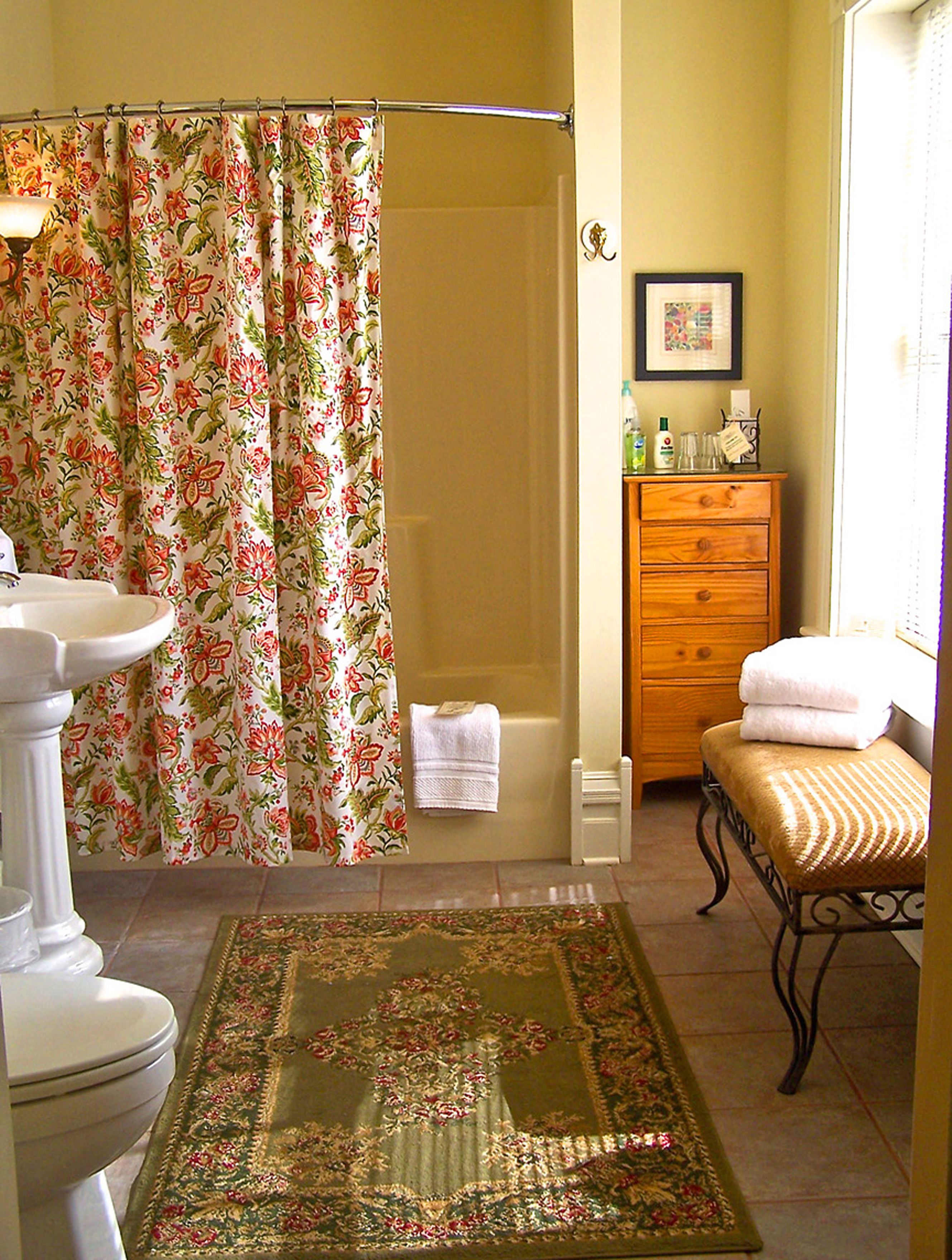 Une salle de bain avec un rideau de douche, un lavabo, une commode en bois, un banc et un tapis.