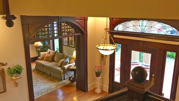 A grand entryway with a wooden staircase, a chandelier, and a view of a cozy living room with a sofa and lamps.