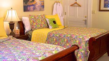 Une chambre à coucher avec deux lits, chacun recouvert d’une couvre-lit aux motifs colorés, une table de chevet avec une lampe et un tableau accroché au mur.