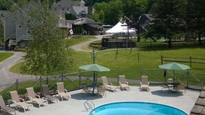 A swimming pool with lounge chairs and umbrellas, surrounded by a grassy area and a mountain backdrop. - Jiminy Peak Mountain Resort (Hancock)