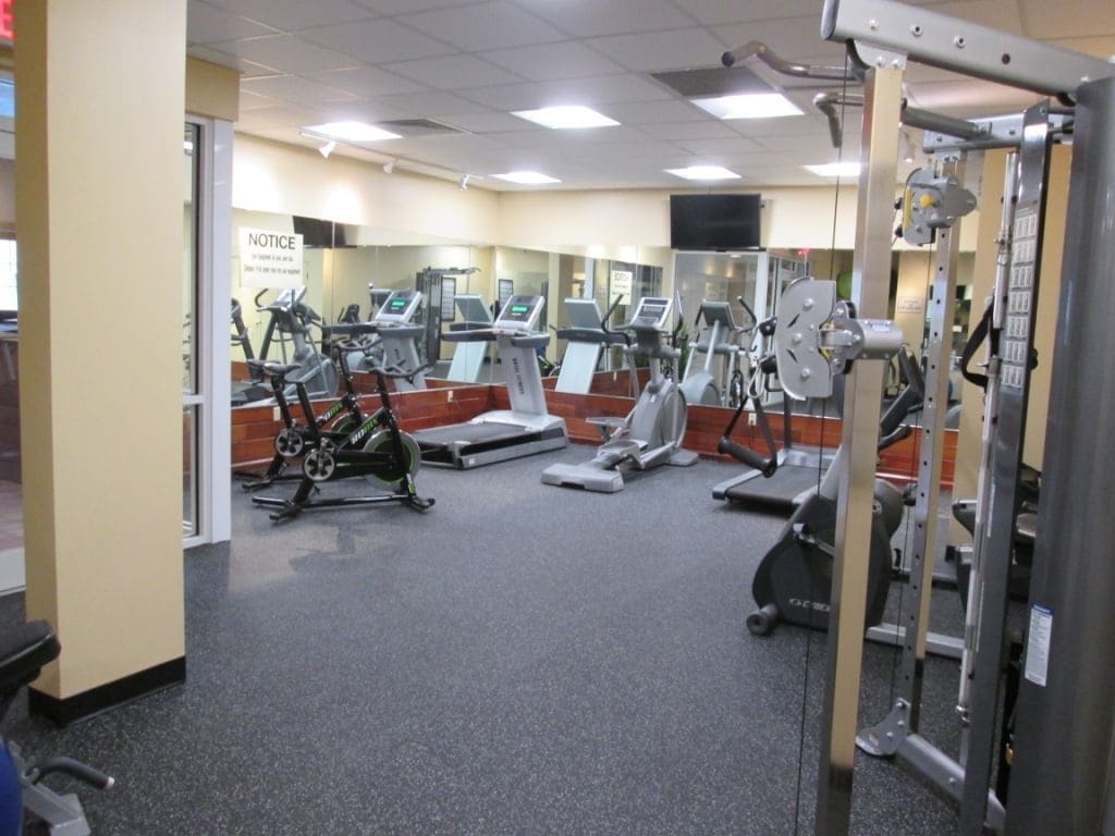 A gym with various exercise machines, a mirrored wall, and a notice board.