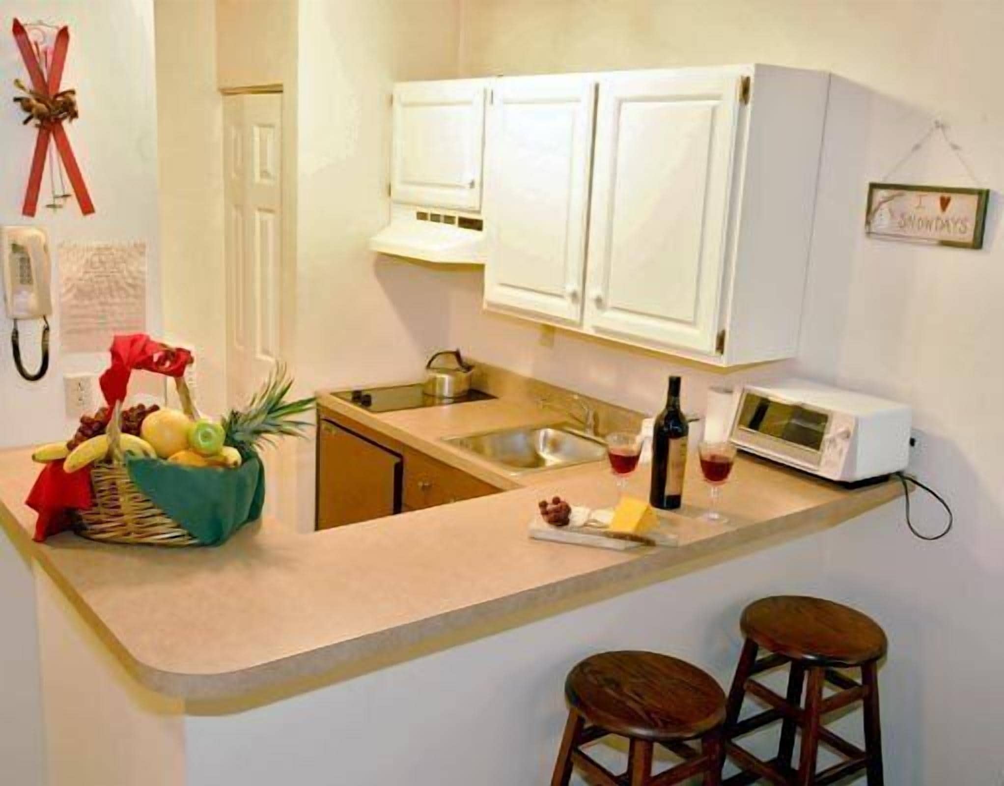 Una cocina con armarios blancos, microondas, una botella de vino y una cesta de fruta.