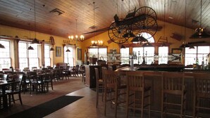 A restaurant interior with wooden tables and chairs, hanging light fixtures, and large windows allowing natural light. - Jiminy Peak Mountain Resort (Hancock)