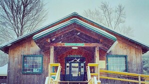 A wooden cabin with a porch and steps leading to a door, surrounded by snow. - Jiminy Peak Mountain Resort (Hancock)