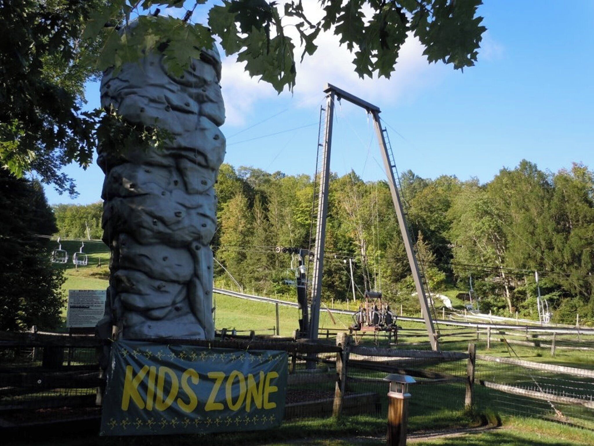 Une formation rocheuse sur laquelle on peut voir un panneau indiquant une « ZONE POUR ENFANTS », une balançoire et une zone délimitée par une clôture, avec des arbres en arrière-plan.