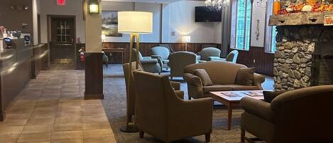 A hotel lobby with a reception desk, seating area with sofas and armchairs, a stone fireplace, and a television mounted on the wall.