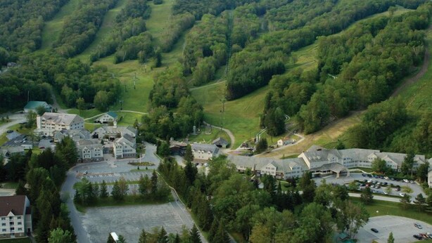 A resort with multiple buildings, a parking area, and a mountainous backdrop. - Jiminy Peak Mountain Resort (Hancock)