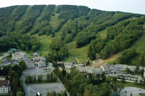 A resort with multiple buildings, a parking area, and a mountainous backdrop. - Jiminy Peak Mountain Resort (Hancock)