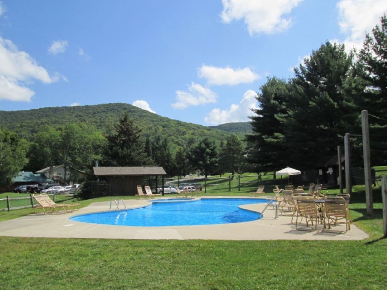 A swimming pool with lounge chairs and a pavilion in a grassy area with a mountain backdrop.
