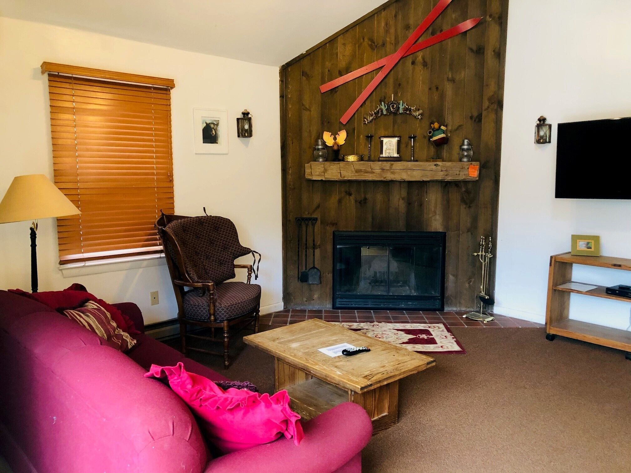 Un salon chaleureux avec une cheminée, un mur en bois, un fauteuil rouge, un canapé rose et un téléviseur.