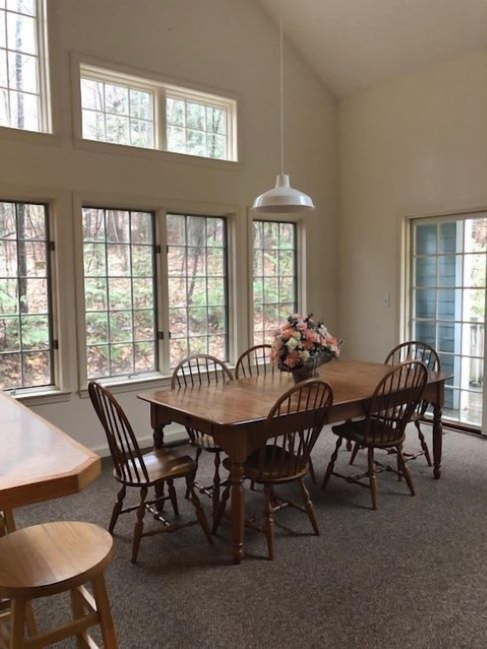 Une salle à manger avec une table et des chaises en bois, de grandes fenêtres et un luminaire suspendu.