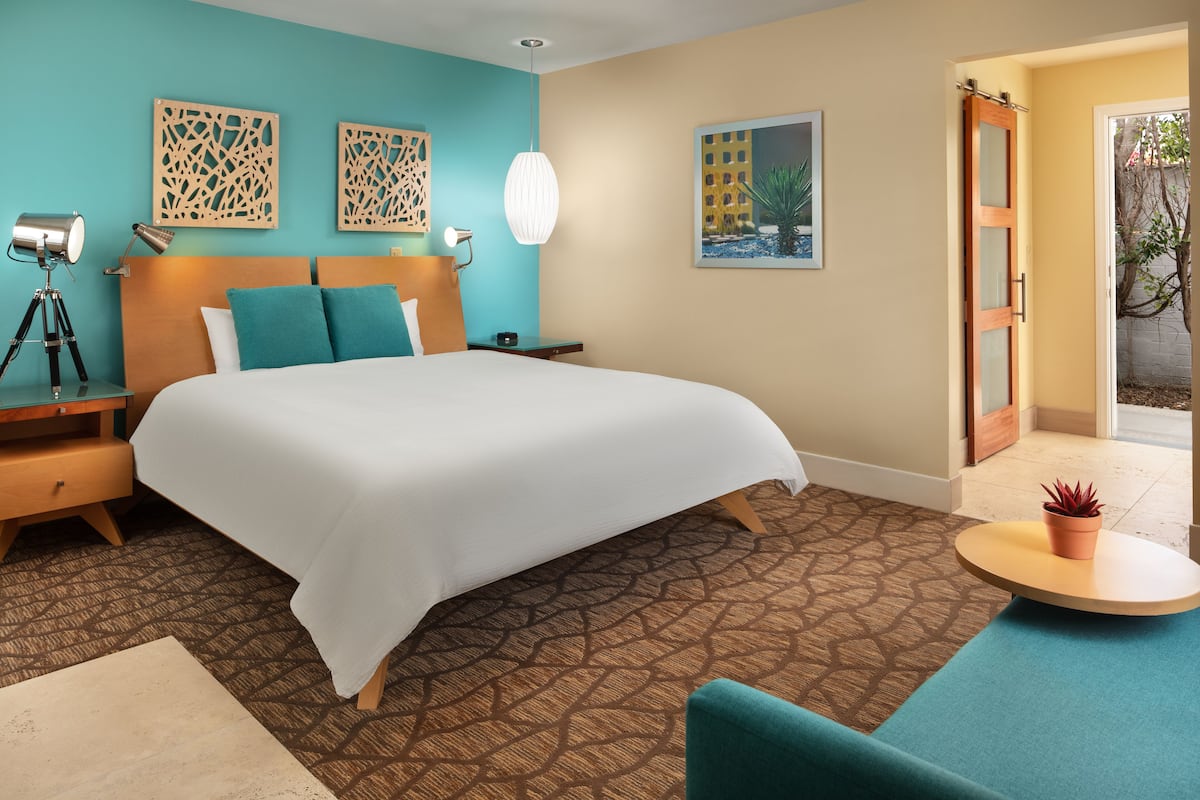 A hotel room with a large bed, a desk, a lamp, and a potted plant.