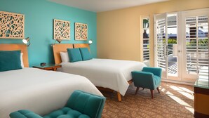 Une chambre d’hôtel avec deux lits, des fauteuils de couleur turquoise, une tête de lit en bois et une moquette à motifs.