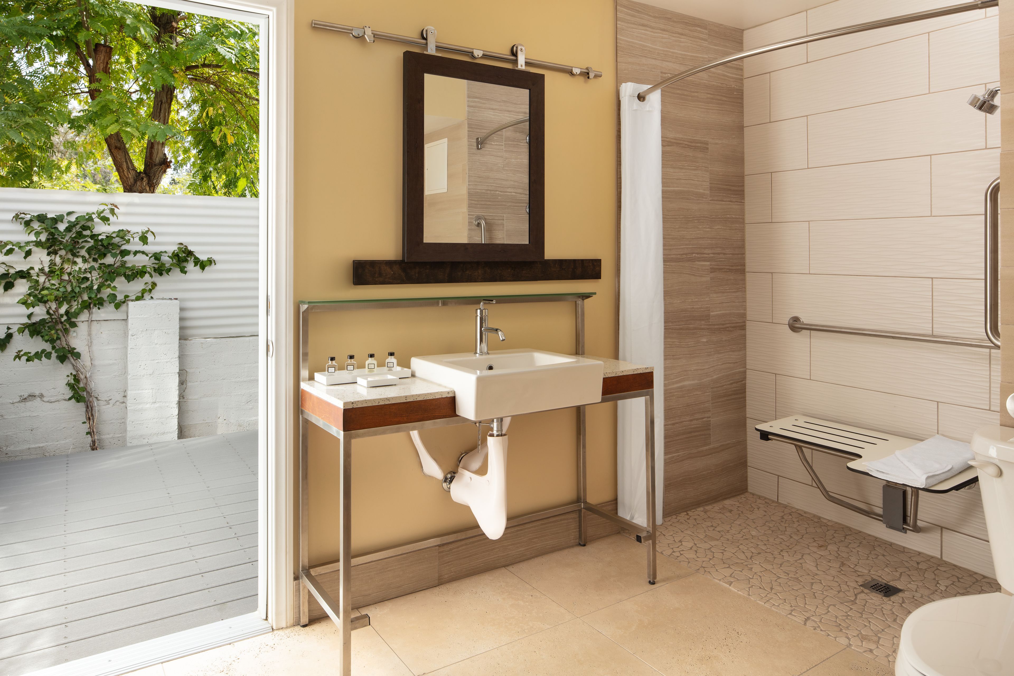 A modern bathroom with a glass shelf holding toiletries, a shower with a glass door, and a toilet with a grab bar.