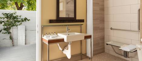 A modern bathroom with a glass shelf holding toiletries, a shower with a glass door, and a toilet with a grab bar.