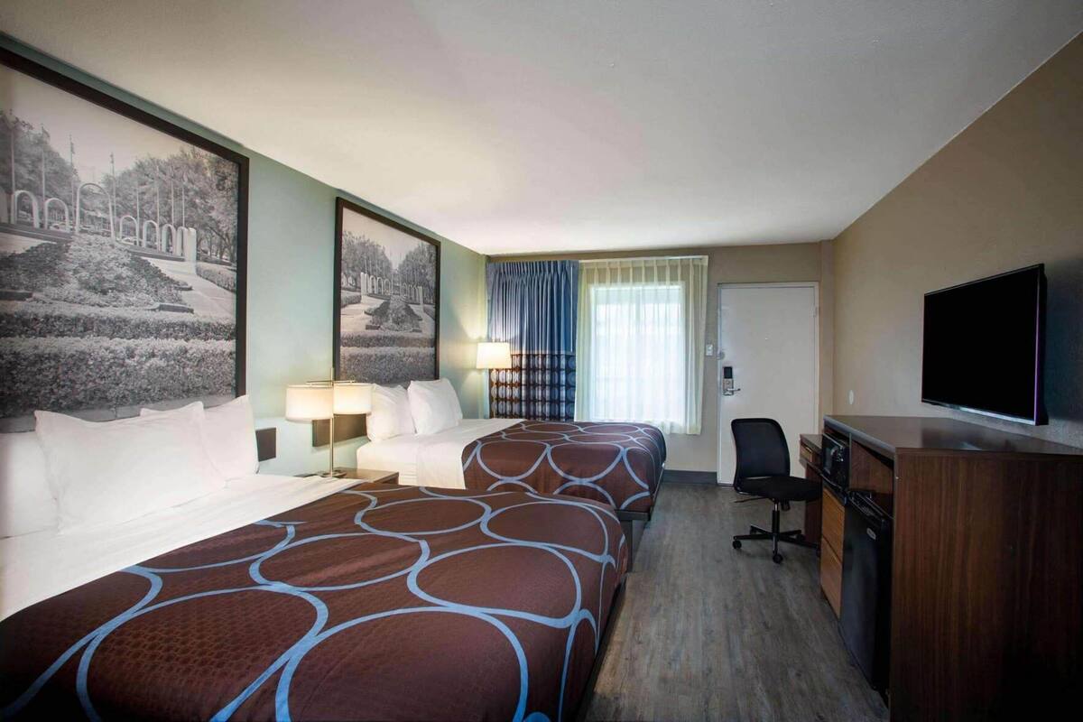 A hotel room with two beds, a desk, a television, and a window with curtains.