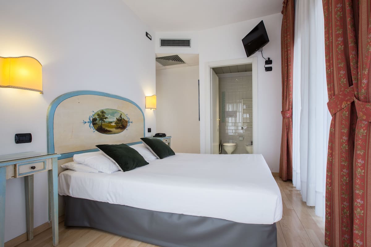 A bedroom with a bed, bedside table, lamp, and a painting on the wall.