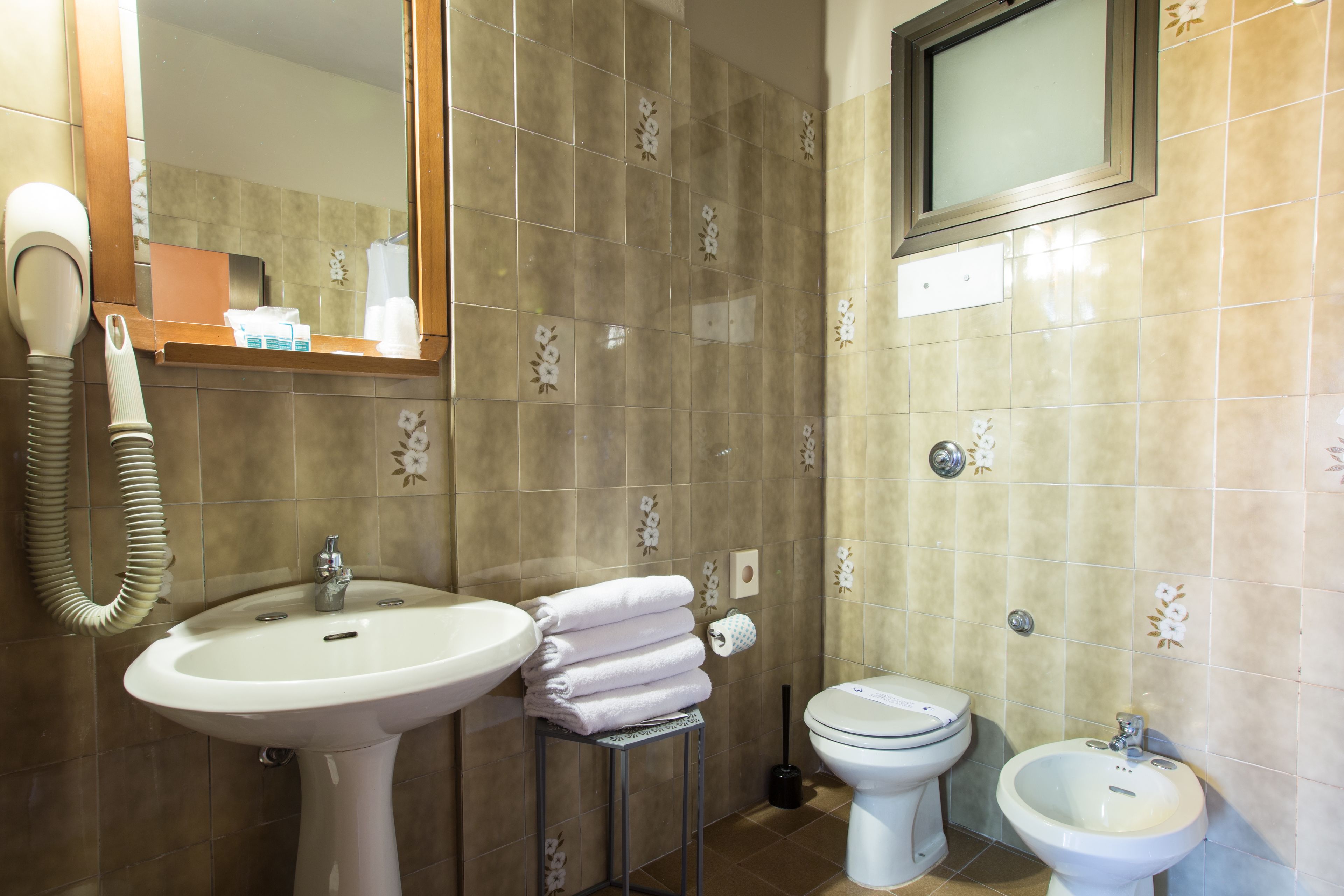 A bathroom with a sink, toilet, bidet, and a hairdryer.