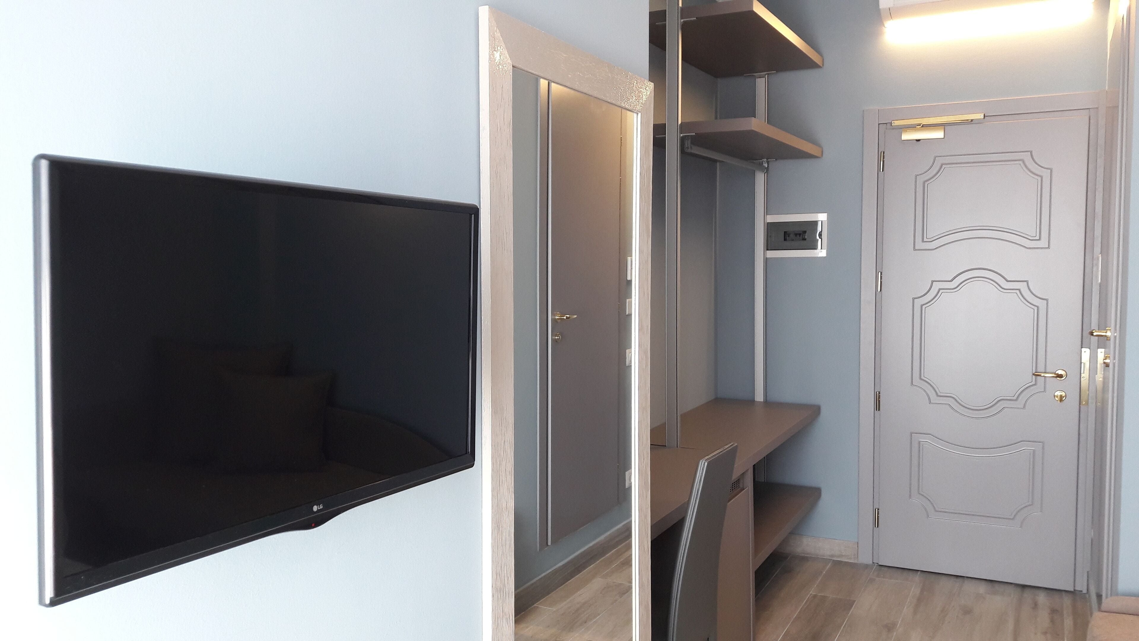 Ein Zimmer mit einem an der Wand befestigten Fernseher, einer Tür mit dekorativer Verkleidung und einem Regal.