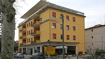 Een geel gebouw met balkons en een bord met Hotel Ariston erop.