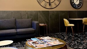 A modern lounge area with a round coffee table covered with magazines, a sofa, and two chairs. There are three clocks on the wall and two pendant lights. - Hotel Ariston (Mestre)