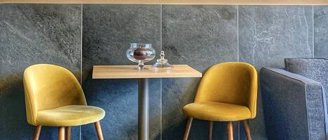Um interior moderno com um relógio de engrenagens fixado na parede, duas cadeiras amarelas, uma mesa pequena com um recipiente de vidro e um chão de mármore.
